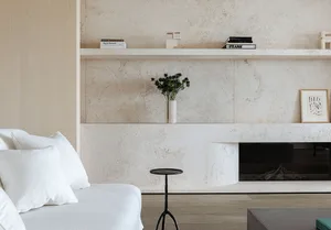 A minimalist living room with white furniture, a concrete fireplace, and a wooden floor.