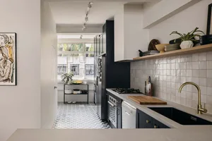 A modern kitchen with white tiles on the backsplash, black cabinets, and a gold faucet.