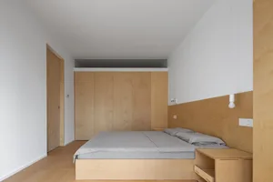 Modern minimalist bedroom with wood paneling, bed, and bedside table.