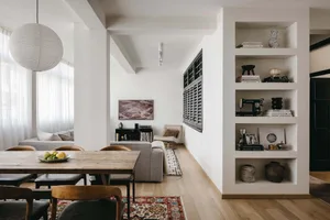 Modern minimalist living room with a wooden table, shelves, and a couch, featuring a cozy atmosphere with a mix of contempora