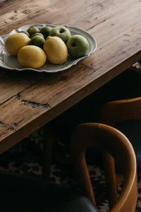 A rustic wooden table with a white plate containing lemons and apples.