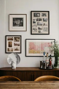A living room with a collection of framed photographs on the wall and a wooden credenza with bottles and a tray of drinks.