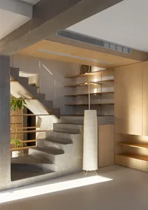 Industrial-style staircase crafted from concrete and accompanied by minimalist shelving and a floor lamp.