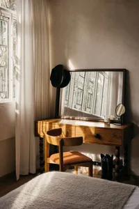 A modern bedroom featuring a wooden console table with a large mirror, a wooden chair with an orange cushion, and a pair of b
