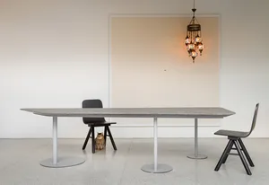 A modern interior with a desk made of concrete, two wooden chairs, a colorful hanging light fixture, and a cat sitting undern