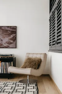 A modern leather chair with a fluffy pillow in a room with white walls and a wooden floor.