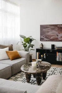 A modern living room with a gray sectional sofa adorned with decorative pillows, a round marble coffee table, and a dark book
