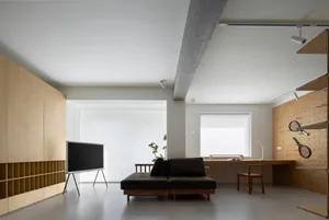 A modern minimalist living room with a black flat-screen TV on a stand, a dark brown sectional sofa, and a wooden desk with a
