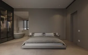 A modern, minimalist bedroom with dark interior design featuring a platform bed, wooden floors, and a glass-walled bathroom w