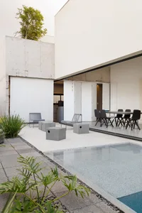 A minimalist patio with concrete furniture and a swimming pool, with a modern building in the background.