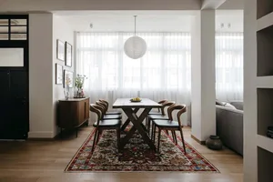 A modern dining room features a wooden table, patterned rug, and wooden flooring.