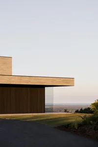 Modern house with large glass walls and wooden accents, set against the backdrop of a clear sky and distant landscape.