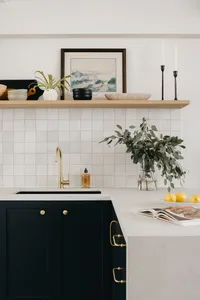 A modern, minimalist kitchen with black cabinets, concrete countertops, and a floating wood shelf above the sink.