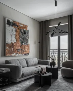 A modern minimalist living room featuring a textured canvas wall art, a comfortable grey sofa, black side tables, and a large