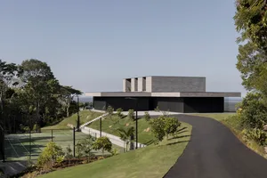 A modern residential house with a concrete exterior and a tennis court in the foreground.