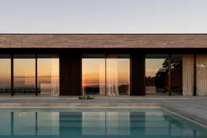 A modern residential exterior featuring large glass windows and a concrete structure.