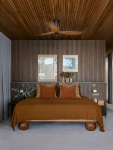 A minimalist bedroom with wooden walls, furniture, and a ceiling fan.