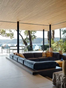 A modern living room featuring wooden floors, large glass windows overlooking a picturesque marina, and stone furniture.