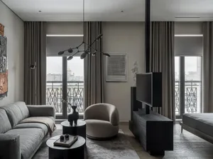 Modern living room featuring a gray sofa, a beige armchair, and a dark TV stand with a large screen and speakers.