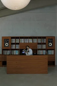 A minimalist reading nook with a wooden table and shelves filled with books, set against a concrete wall and ceiling with a s