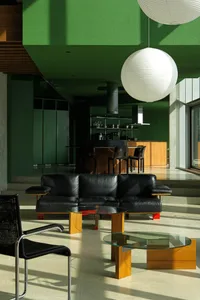 A modern living room with a black leather sofa, wooden coffee table, and green walls.