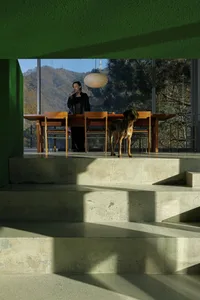 A modern house with concrete stairs and wooden railings, featuring a dog and a person drinking wine.