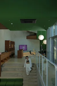 A modern living room with concrete cladding and green accent wall, where a woman walks up the stairs.