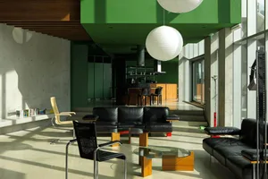 Modern living room featuring a sleek black couch, metal chairs, concrete flooring, and pendant lamps.