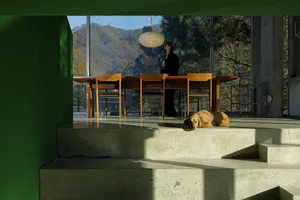 A modern living room with concrete stairs, wooden dining table, and a dog lying on the stairs.