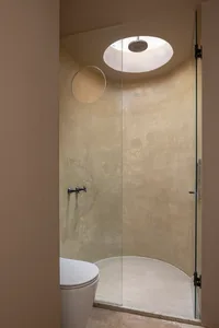A minimalist bathroom featuring a concrete shower enclosure, circular skylight, and a white toilet.
