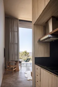 A minimalist residential kitchen featuring wood elements and a view of the outdoors through sheer curtains.