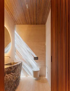 Modern bathroom featuring a stone tile floor and walls, sleek fixtures, and a wooden door with vertical slats.