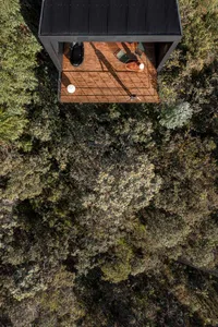 A modern outdoor space with a wooden floor and black roof surrounded by dense greenery.