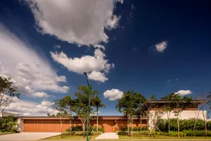 Modern house exterior with concrete and wooden elements, featuring a driveway and lush green landscape.
