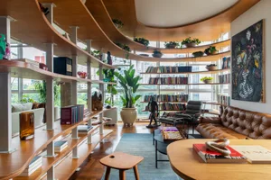 A modern living room featuring curved wooden shelves and a variety of books and plants.