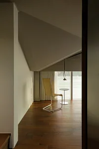 A modern living room with a wooden floor, featuring a single wicker chair and a small round table.