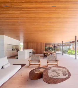 Modern living room with wooden floor and furniture, featuring a white sofa, woven chairs, and a coffee table.