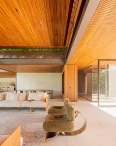 Modern living room with wood ceiling and marble floor, featuring contemporary furniture and a view of the outdoor greenery.