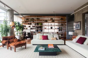 A minimalist living room with a wooden couch, concrete walls, and glass shelves.