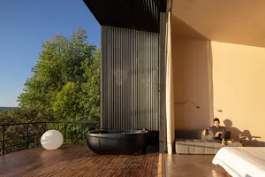 Modern residential interior space featuring wooden flooring, concrete walls, metal columns, and a glass door leading to an ou