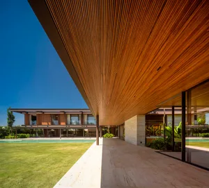 Modern residential building with a wooden roof and concrete pool area surrounded by lush greenery.