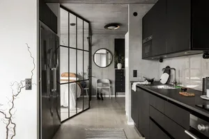 Industrial-inspired black kitchen with concrete panel walls, framed glass walls connecting to bedroom, and black steel kitche