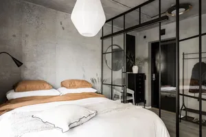 Minimalist bedroom with glass walls and wood furniture, featuring a concrete texture wall and white bedding.