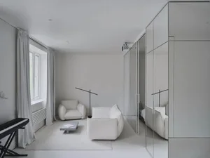 A minimalist living room with white furniture and walls, featuring a sofa, armchair, and small table.