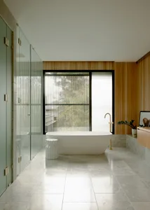 A modern bathroom with concrete flooring, a freestanding bathtub, a wooden accent wall, and a frosted glass shower.