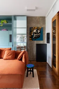 A modern industrial living room showcasing concrete, walnut, and orange sofa, with a concrete accent wall and wooden flooring