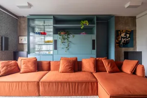 Modern interior design featuring a large, orange sectional sofa in a living room setting with a blue storage unit and concret