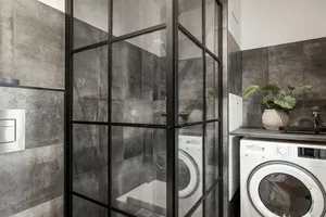 A modern laundry room featuring concrete walls and glass-enclosed shower stall.