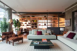 A modern living room features a concrete plant shelf, white sofas with colorful pillows, and a metal and green stone coffee t
