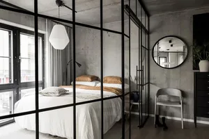 Modern minimalist bedroom with concrete walls, glass door, and wooden floor.